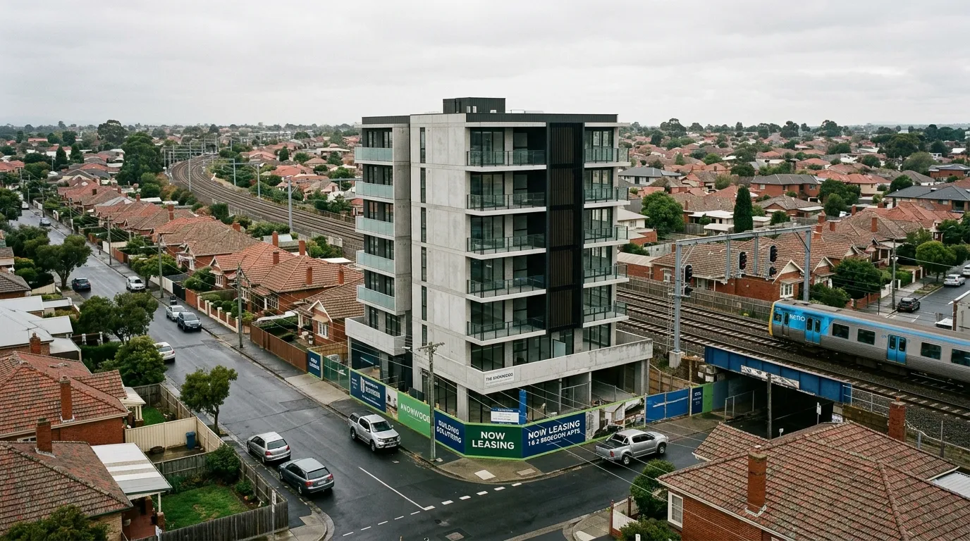 A single new mid-rise apartment building standing among interwar brick houses beside a Melbourne railway line